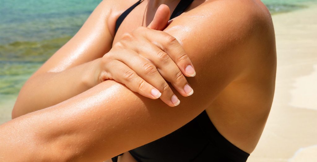Jovem na praia aplicando protetor solar para prevenir danos à pele e proteger contra queimaduras solares. A conscientização sobre a importância do cuidado com a pele para evitar danos permanentes e promover um estilo de vida saudável.